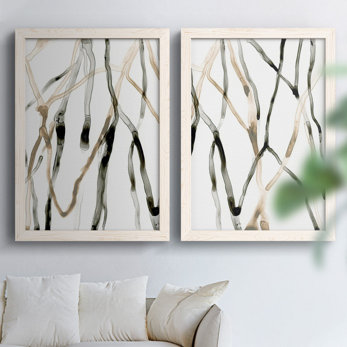 Set of two white barnwood framed canvas prints depicting slender vein-like strokes, transparent overlaps, and open negative space arranged across two complementary compositions above a sofa in a bright living space.