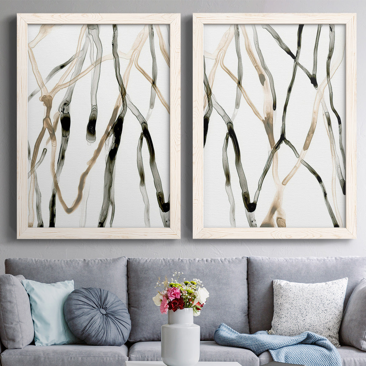 Set of two white barnwood framed canvas prints depicting paired fluid organic abstracts with slender vein-like strokes, transparent overlaps, and open negative space above a sofa in a contemporary living room.