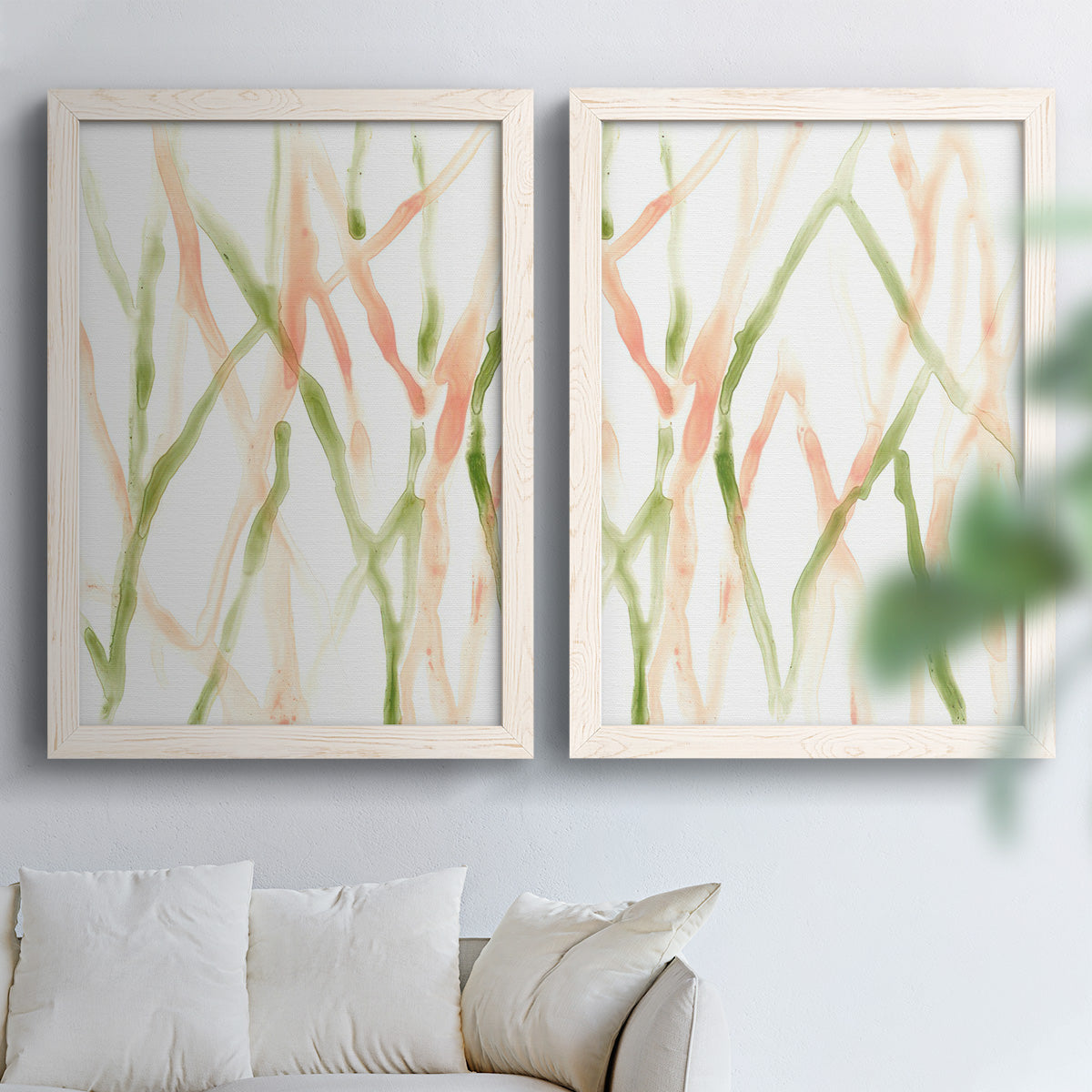 Set of two white barnwood framed canvas prints depicting slender vein-like strokes, transparent overlaps, and open negative space arranged across two complementary compositions above a sofa in a bright living space.