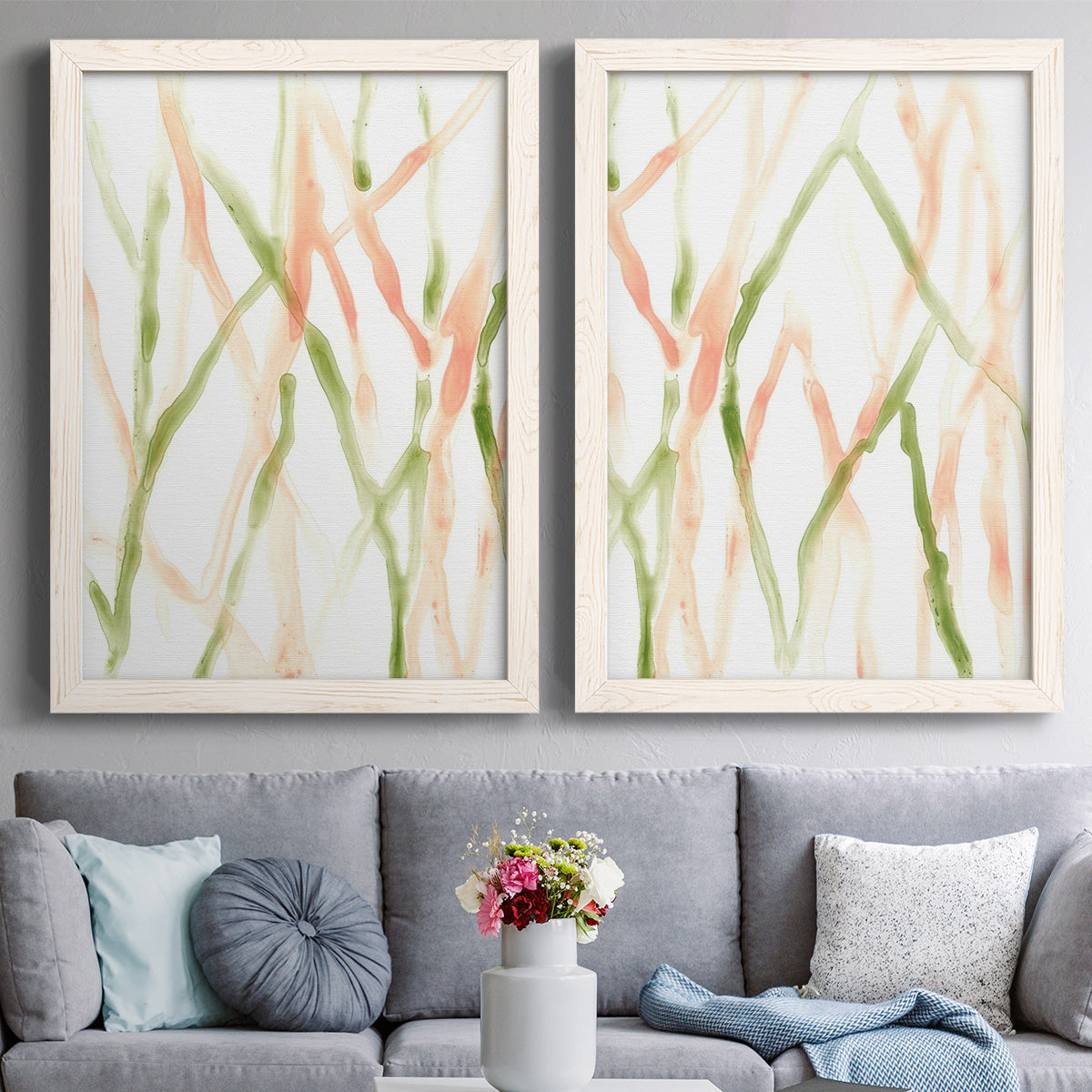Set of two white barnwood framed canvas prints depicting paired fluid organic abstracts with slender vein-like strokes, transparent overlaps, and open negative space above a sofa in a contemporary living room.