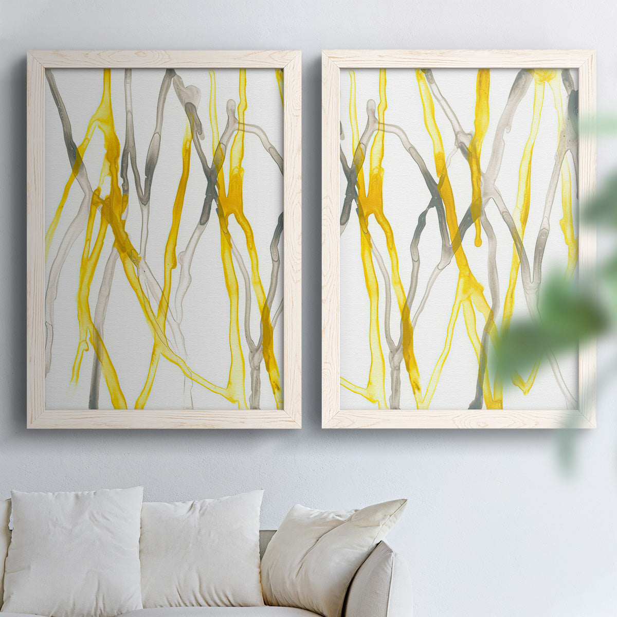 Set of two white barnwood framed canvas prints depicting slender vein-like strokes, transparent overlaps, and open negative space arranged across two complementary compositions above a sofa in a bright living space.