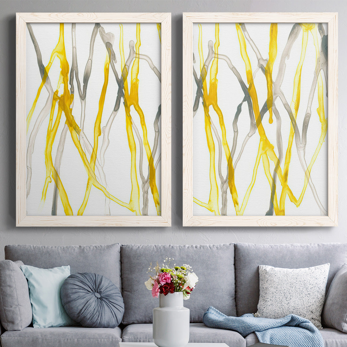 Set of two white barnwood framed canvas prints depicting paired fluid organic abstracts with slender vein-like strokes, transparent overlaps, and open negative space above a sofa in a contemporary living room.