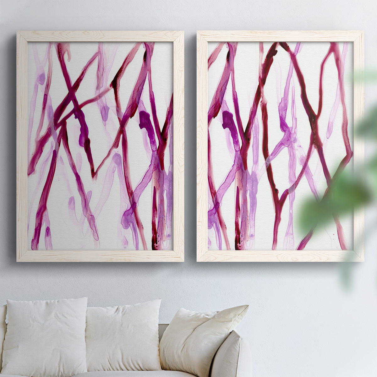 Set of two white barnwood framed canvas prints depicting slender vein-like strokes, transparent overlaps, and open negative space arranged across two complementary compositions above a sofa in a bright living space.