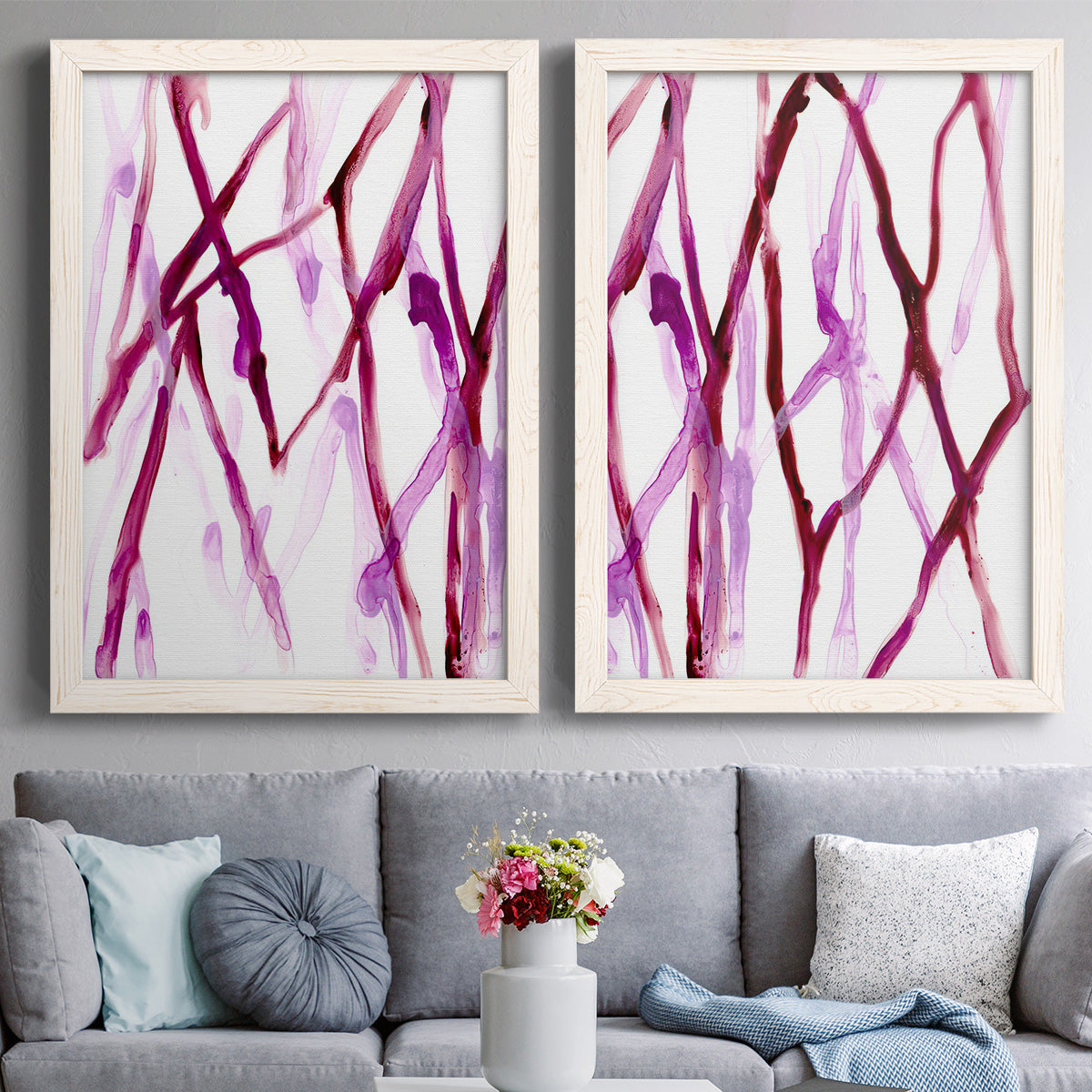 Set of two white barnwood framed canvas prints depicting paired fluid organic abstracts with slender vein-like strokes, transparent overlaps, and open negative space above a sofa in a contemporary living room.