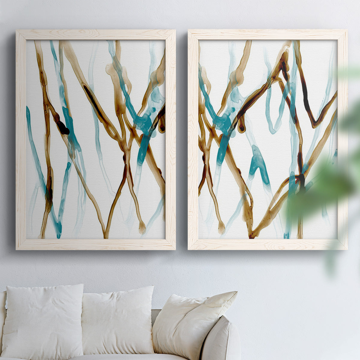 Set of two white barnwood framed canvas prints depicting organic linear forms in aqua brown and black flowing vertically through open white space above a sofa in a bright living space.