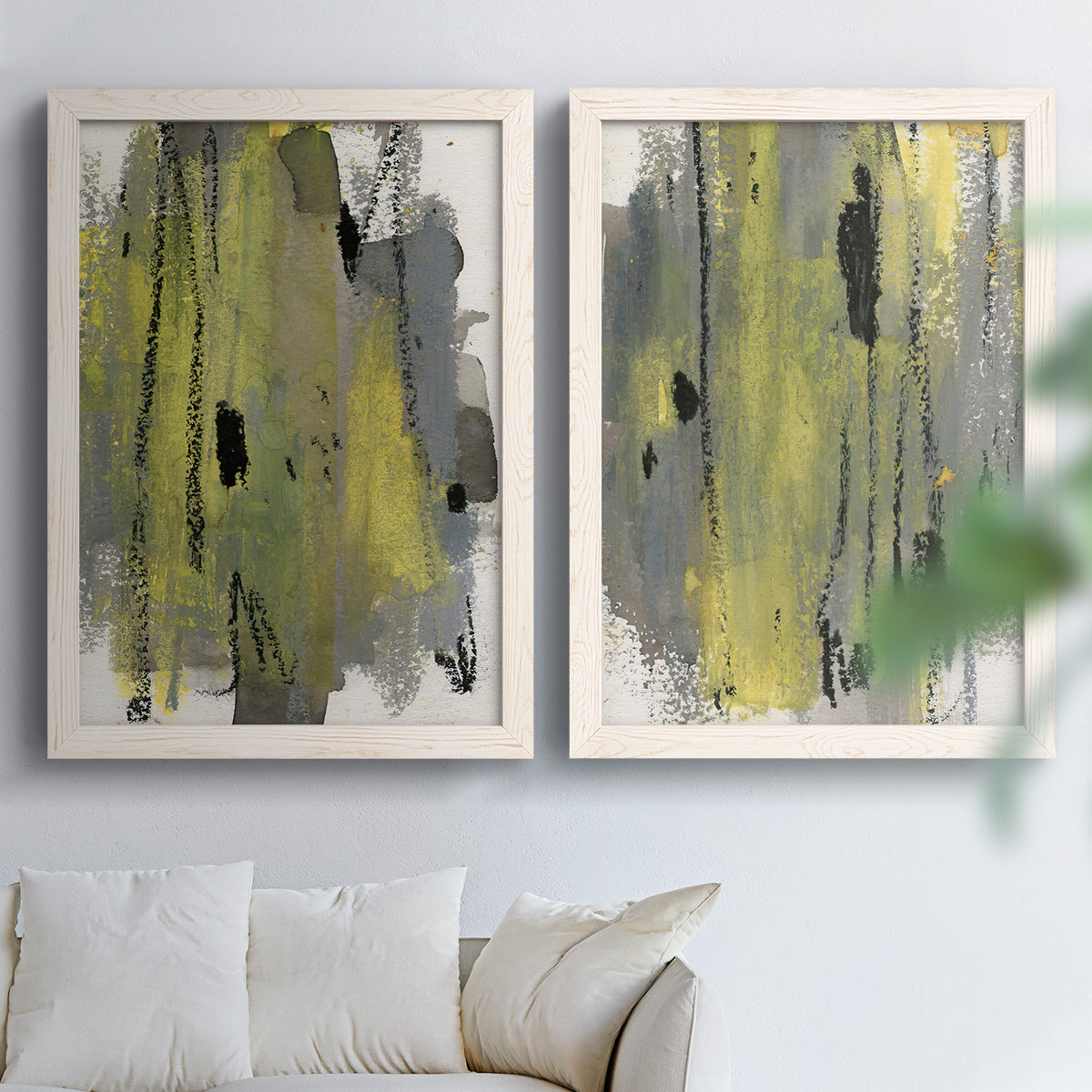 Set of two white barnwood framed canvas prints depicting scraped paint, black accents, and layered gray green rust or yellow fields arranged across two complementary compositions above a sofa in a bright living space.
