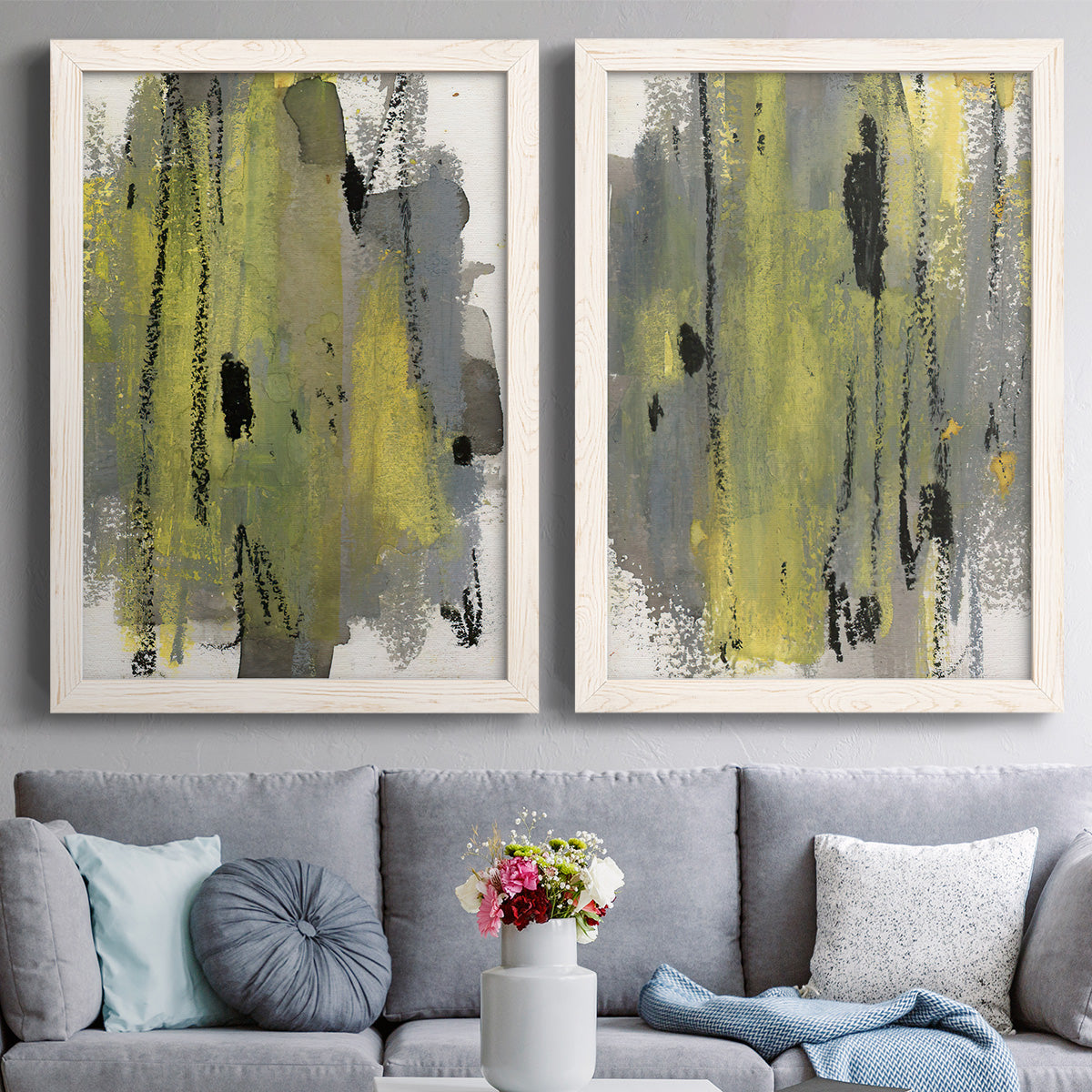 Set of two white barnwood framed canvas prints depicting paired urban mixed-media abstracts with scraped paint, black accents, and layered gray green rust or yellow fields above a sofa in a contemporary living room.