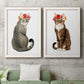 Set of two white barnwood framed canvas prints depicting a coordinated art pair of seated cats wearing colorful flower crowns rendered as whimsical animal portraits above a sofa in a modern living room.
