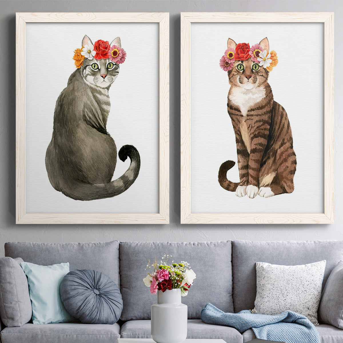 Set of two white barnwood framed canvas prints depicting paired whimsical animal portraits with tabby fur, pink orange and yellow blossoms, and clean white grounds above a sofa in a contemporary living room.