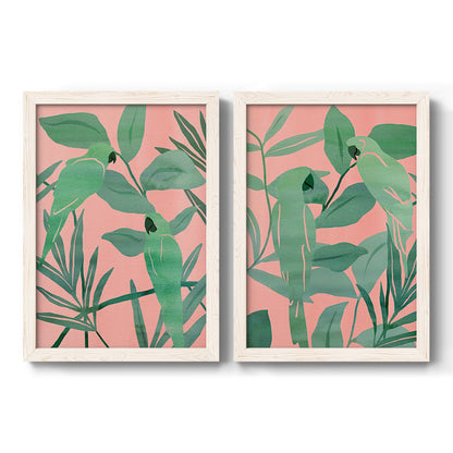 Set of two white barnwood framed canvas prints featuring two bold tropical botanical prints featuring large green tropical leaves on coral-pink grounds.