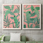 Set of two white barnwood framed canvas prints depicting a coordinated art pair of large green tropical leaves on coral-pink grounds rendered as bold tropical botanical prints above a sofa in a modern living room.