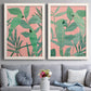 Set of two white barnwood framed canvas prints depicting paired bold tropical botanical prints with overlapping foliage, flat graphic shapes, and high-contrast color above a sofa in a contemporary living room.