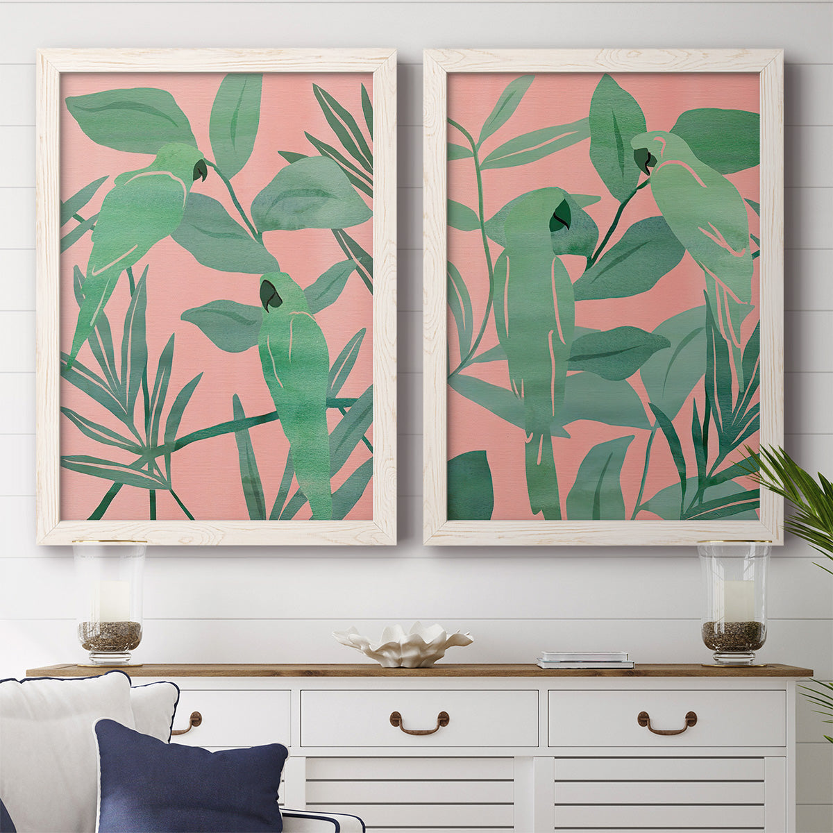 Set of two white barnwood framed canvas prints depicting a coordinated art pair of large green tropical leaves on coral-pink grounds rendered as bold tropical botanical prints above a dining room sideboard.