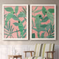 Set of two white barnwood framed canvas prints depicting two bold tropical botanical prints featuring large green tropical leaves on coral-pink grounds above a sideboard in a cozy sitting room.