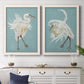 Set of two white barnwood framed canvas prints depicting a coordinated art pair of white herons displaying long windswept feathers rendered as decorative bird illustrations above a dining room sideboard.