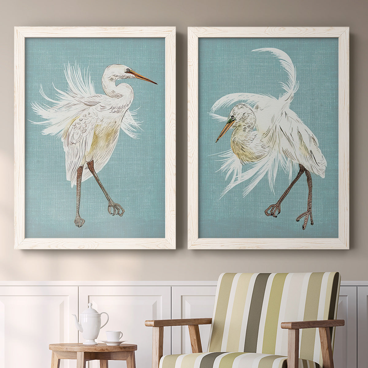 Set of two white barnwood framed canvas prints depicting two decorative bird illustrations featuring white herons displaying long windswept feathers above a sideboard in a cozy sitting room.