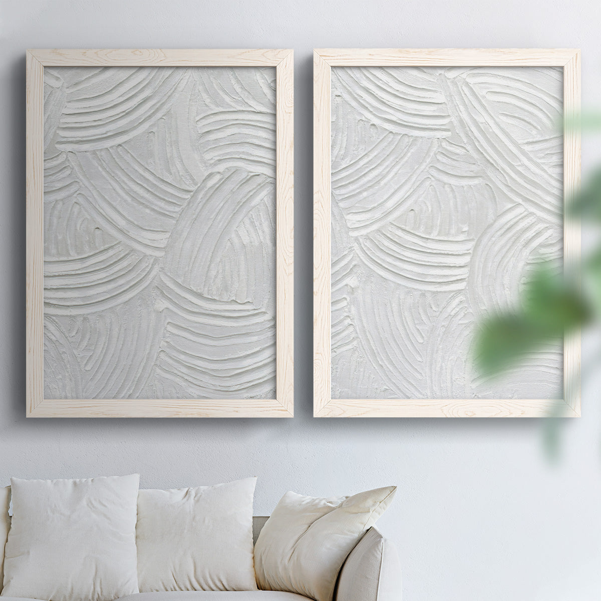 Set of two white barnwood framed canvas prints depicting raised sweeping grooves, soft shadows, and pale stone-like surfaces arranged across two complementary compositions above a sofa in a bright living space.