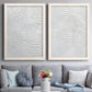 Set of two white barnwood framed canvas prints depicting paired textural monochrome abstracts with raised sweeping grooves, soft shadows, and pale stone-like surfaces above a sofa in a contemporary living room.