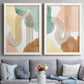 Set of two white barnwood framed canvas prints depicting paired folk-inspired botanical patterns with stylized bouquets, blue block-print forms, and warm white grounds above a sofa in a contemporary living room.