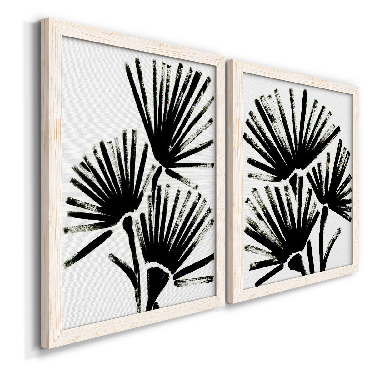 Angled view of a set of two white barnwood framed canvas prints featuring two bold monochrome botanical prints featuring black fan-shaped botanical forms.