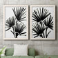 Set of two white barnwood framed canvas prints depicting a coordinated art pair of black fan-shaped botanical forms rendered as bold monochrome botanical prints above a sofa in a modern living room.