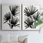 Set of two white barnwood framed canvas prints depicting radiating brush marks, repeated leaf-like fans, and white grounds arranged across two complementary compositions above a sofa in a bright living space.