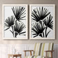 Set of two white barnwood framed canvas prints depicting two bold monochrome botanical prints featuring black fan-shaped botanical forms above a sideboard in a cozy sitting room.