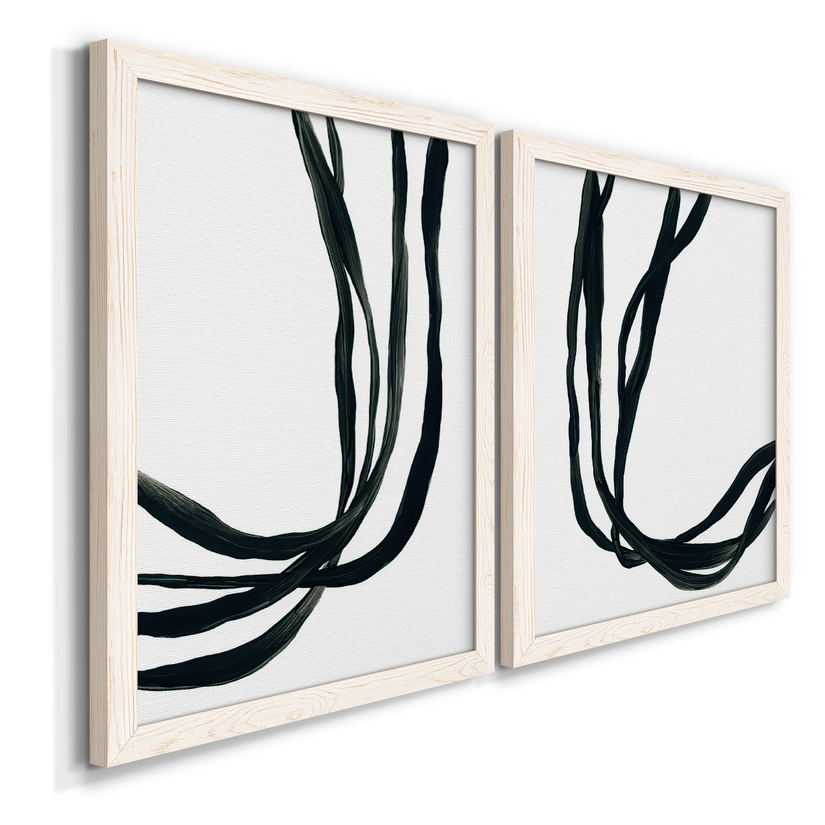 Angled view of a set of two white barnwood framed canvas prints featuring two minimalist gestural line abstracts featuring flowing black ribbon-like lines.