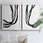 Set of two white barnwood framed canvas prints depicting thick looping strokes, white space, and elegant vertical movement arranged across two complementary compositions above a sofa in a bright living space.