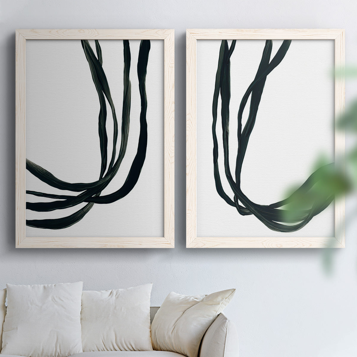 Set of two white barnwood framed canvas prints depicting thick looping strokes, white space, and elegant vertical movement arranged across two complementary compositions above a sofa in a bright living space.