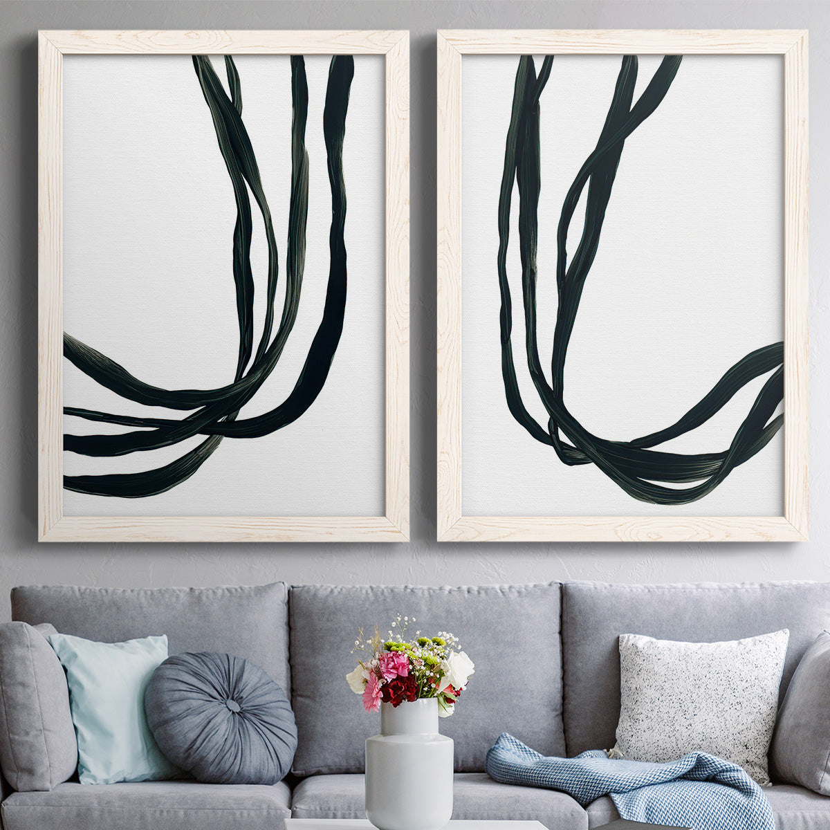 Set of two white barnwood framed canvas prints depicting paired minimalist gestural line abstracts with thick looping strokes, white space, and elegant vertical movement above a sofa in a contemporary living room.