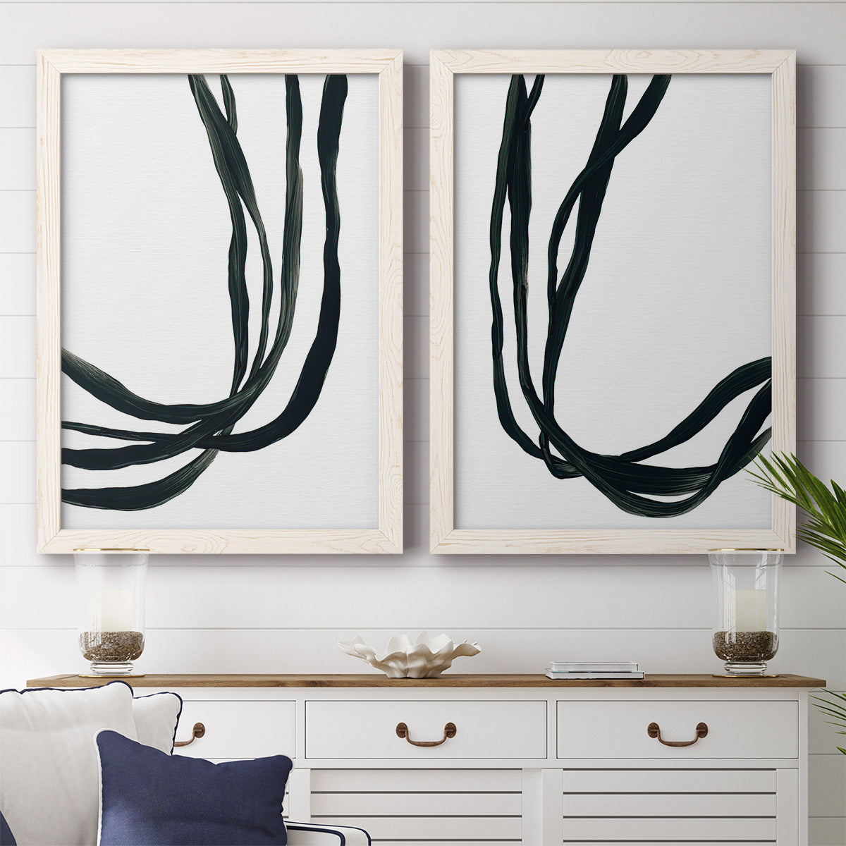 Set of two white barnwood framed canvas prints depicting a coordinated art pair of flowing black ribbon-like lines rendered as minimalist gestural line abstracts above a dining room sideboard.