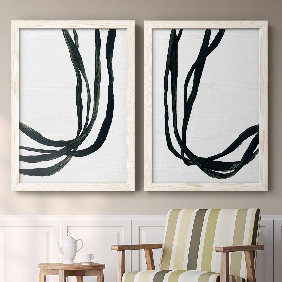 Set of two white barnwood framed canvas prints depicting two minimalist gestural line abstracts featuring flowing black ribbon-like lines above a sideboard in a cozy sitting room.