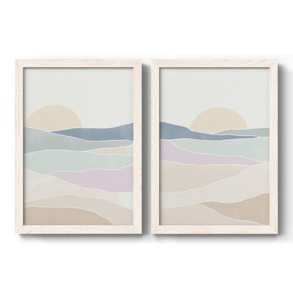 Set of two white barnwood framed canvas prints featuring two minimalist abstract landscapes featuring layered pastel waves beneath a pale setting sun.