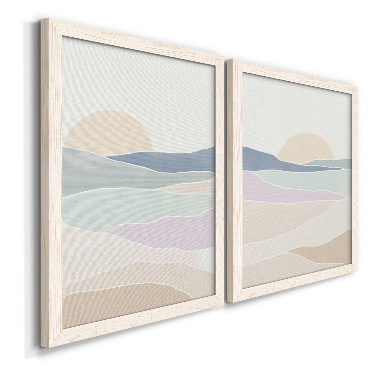 Angled view of a set of two white barnwood framed canvas prints featuring two minimalist abstract landscapes featuring layered pastel waves beneath a pale setting sun.