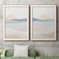 Set of two white barnwood framed canvas prints depicting a coordinated art pair of layered pastel waves beneath a pale setting sun rendered as minimalist abstract landscapes above a sofa in a modern living room.