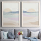 Set of two white barnwood framed canvas prints depicting paired minimalist abstract landscapes with soft blue lavender beige and cream bands with a simple horizon above a sofa in a contemporary living room.