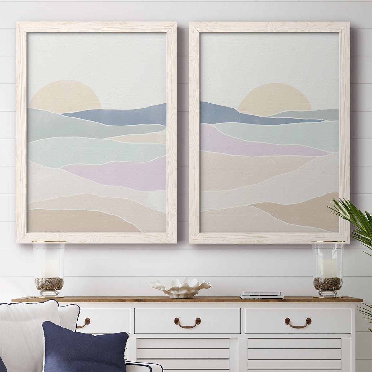 Set of two white barnwood framed canvas prints depicting a coordinated art pair of layered pastel waves beneath a pale setting sun rendered as minimalist abstract landscapes above a dining room sideboard.