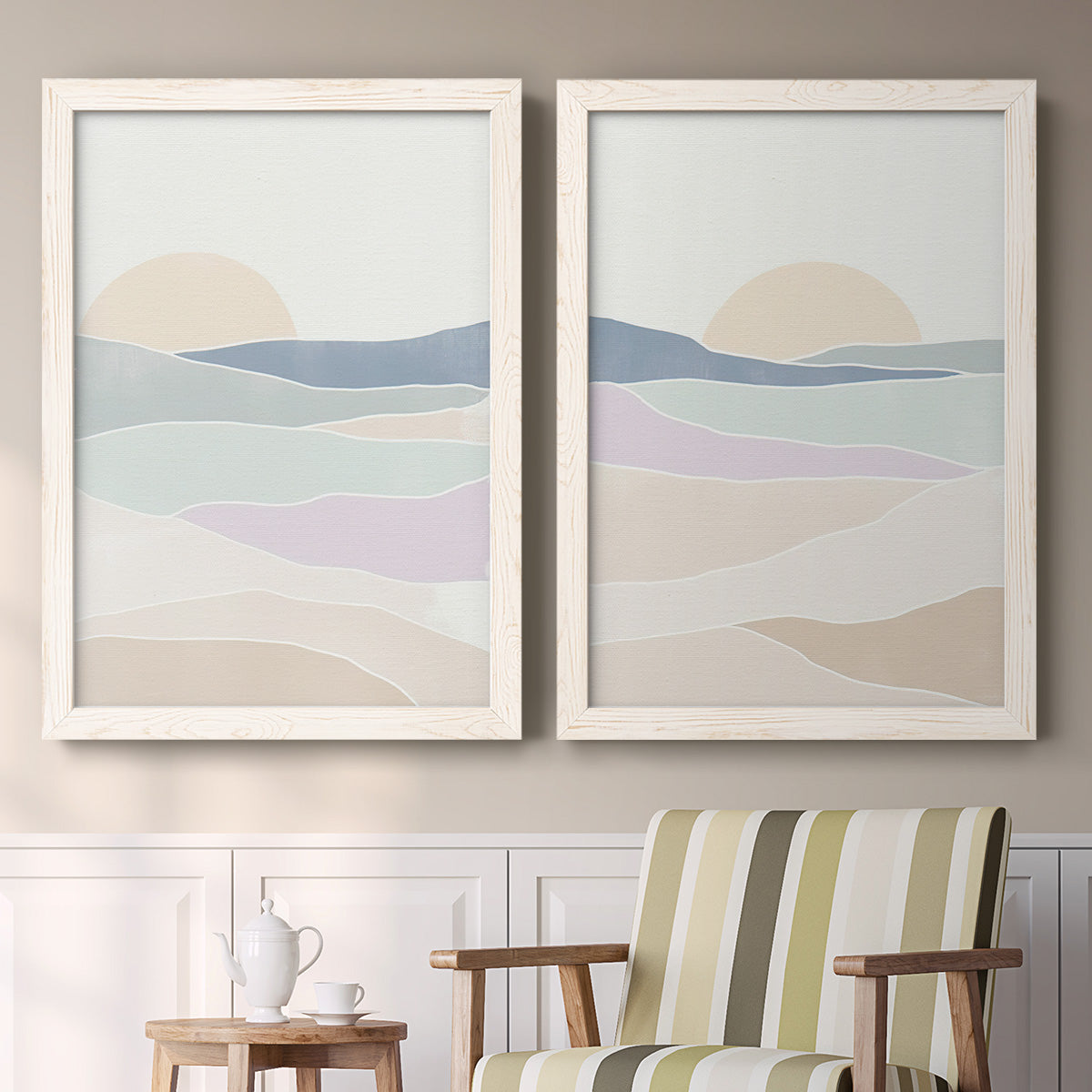 Set of two white barnwood framed canvas prints depicting two minimalist abstract landscapes featuring layered pastel waves beneath a pale setting sun above a sideboard in a cozy sitting room.