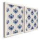 Angled view of a set of two white barnwood framed canvas prints featuring two repeating blue floral patterns with stylized bouquets arranged across warm white backgrounds.