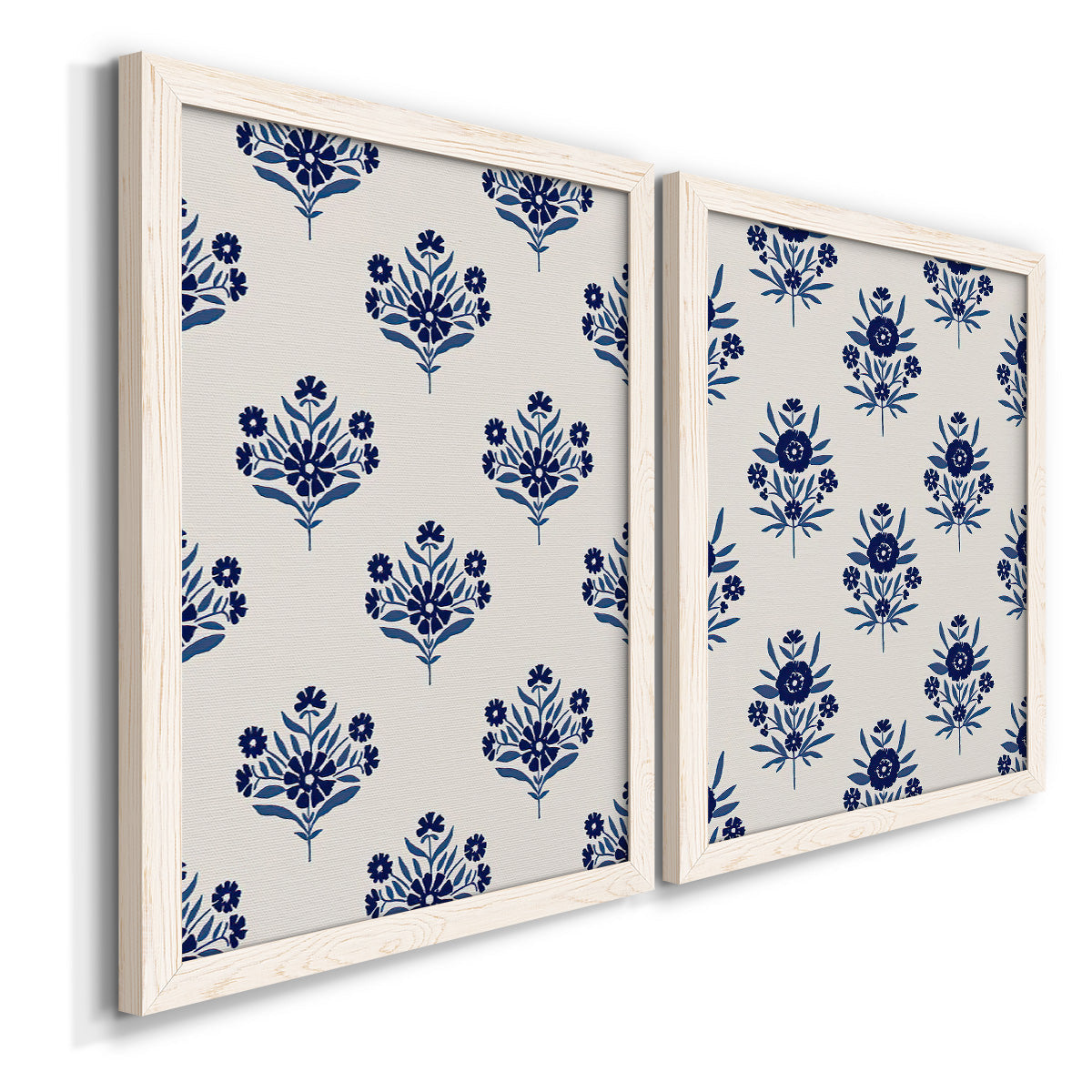 Angled view of a set of two white barnwood framed canvas prints featuring two repeating blue floral patterns with stylized bouquets arranged across warm white backgrounds.