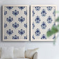Set of two white barnwood framed canvas prints depicting decorative folk inspired florals rendered in deep blue on soft cream fields above a sofa in a bright living space.
