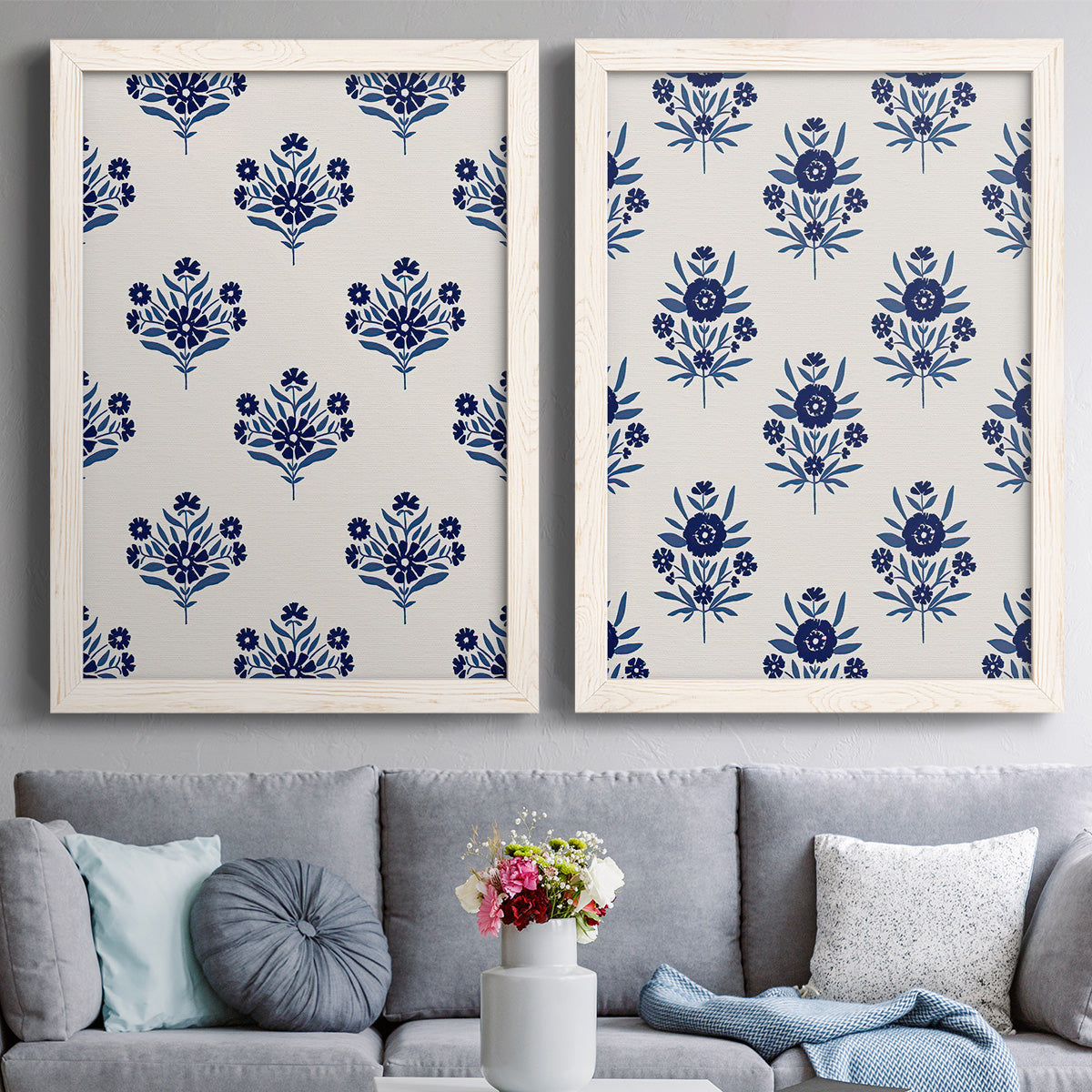 Set of two white barnwood framed canvas prints depicting graphic block print bouquets with symmetrical leaves blossoms and bold indigo coloring above a sofa in a contemporary living room.