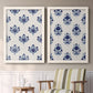Set of two white barnwood framed canvas prints depicting two repeating blue floral patterns with stylized bouquets arranged across warm white backgrounds above a sideboard in a cozy sitting room.