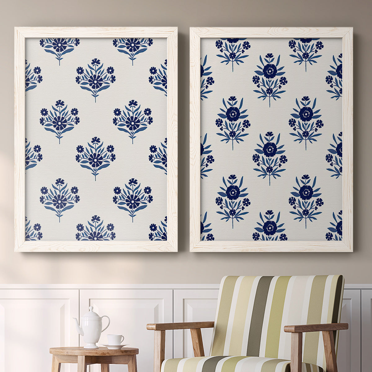 Set of two white barnwood framed canvas prints depicting two repeating blue floral patterns with stylized bouquets arranged across warm white backgrounds above a sideboard in a cozy sitting room.