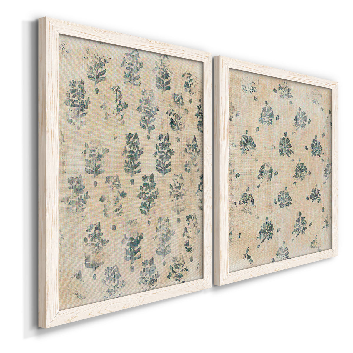 Angled view of a set of two white barnwood framed canvas prints featuring two weathered block-print patterns featuring small repeating blue floral motifs.