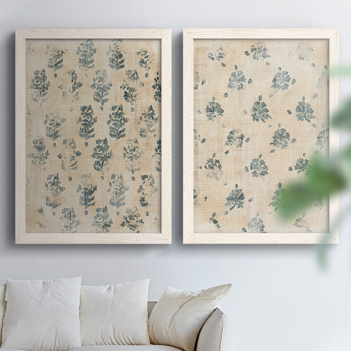 Set of two white barnwood framed canvas prints depicting distressed cream grounds, indigo stamps, and antique textile character arranged across two complementary compositions above a sofa in a bright living space.