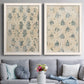 Set of two white barnwood framed canvas prints depicting paired weathered block-print patterns with distressed cream grounds, indigo stamps, and antique textile character above a sofa in a contemporary living room.