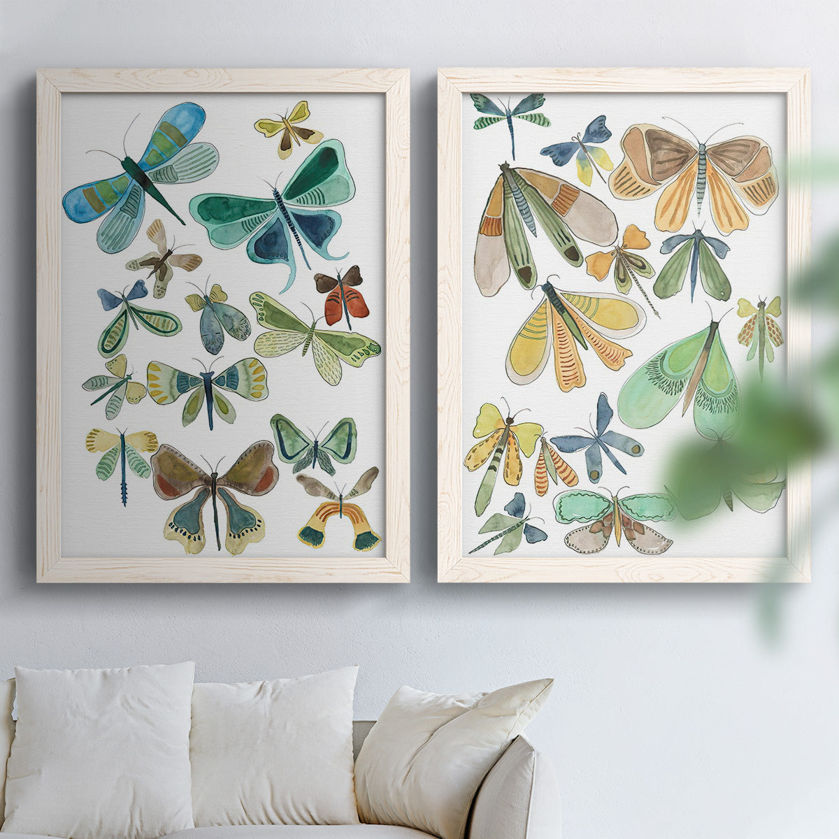 Set of two white barnwood framed canvas prints depicting patterned wings, leafy accents, and softly vintage natural-history styling arranged across two complementary compositions above a sofa in a bright living space.