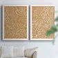 Set of two white barnwood framed canvas prints depicting leaf-like contours, flat warm backgrounds, and repeated flowing shapes arranged across two complementary compositions above a sofa in a bright living space.